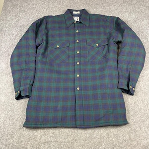May include: A long-sleeve button-down shirt featuring a dark blue and forest green plaid pattern. The shirt includes a pointed collar, two chest pockets with buttoned flaps, and light-colored buttons running down the center front and on the cuffs.