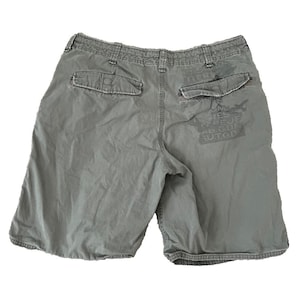 May include: A pair of olive green cargo shorts. The shorts have two back pockets and a faded graphic print on the back. The shorts are made of a durable fabric and have a relaxed fit.