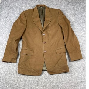 May include: A solid brown blazer featuring a notched lapel, three front buttons, and two flap pockets at the waist. The garment has long sleeves and a visible olive green interior lining, constructed with a structured collar and shoulder design.