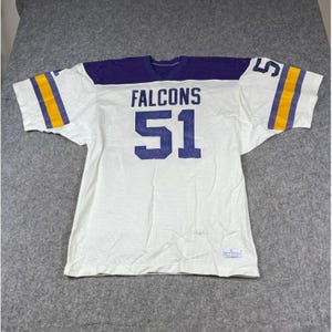 May include: A white mesh football jersey with purple shoulders and sleeves. The front features the word FALCONS in purple letters above the number 51 in large purple numerals. The sleeves have yellow and purple stripes and the number 51.