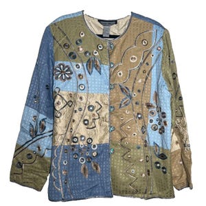 May include: A patchwork jacket in shades of blue, tan, and olive green. The jacket features embroidered floral and geometric designs. The jacket has long sleeves and a round neckline.