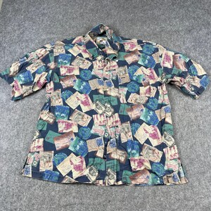 May include: A short-sleeved button-down shirt featuring a dark blue base with an all-over print of vintage-style postage stamps, envelopes, and circular postmarks in shades of green, red, and tan. The shirt includes a collar and a front placket.
