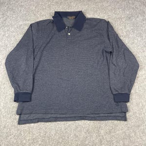 May include: A long-sleeve polo shirt in a dark navy blue and black micro-check pattern. The shirt features a solid navy blue collar, a two-button placket with white buttons, and solid navy blue cuffs. A small embroidered logo is visible on the hem.