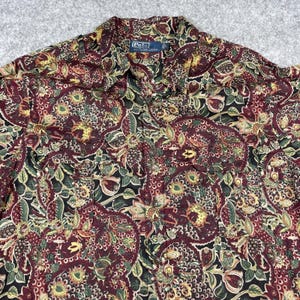 May include: A button-down shirt with a paisley pattern in burgundy, green, and yellow. The shirt has a collar and the Polo by Ralph Lauren label is visible. The fabric has a floral design.