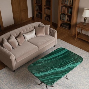 Op de afbeelding: Een woonkamer met een beige bank en kussens, een groene malachiet salontafel en houten boekenkasten. De kamer heeft een lichtblauw patroonkleed en een houten bijzettafel met een lamp. De salontafel is ongeveer 120 cm lang.