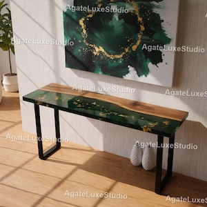 Op de afbeelding: Een moderne consoletafel met een houten blad met levende rand en een groene epoxyharsinleg met gouden accenten. De tafel wordt ondersteund door zwarte metalen poten. De tekst "AgateLuxeStudio" is zichtbaar.