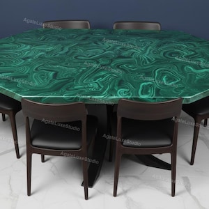 Op de afbeelding: Een achthoekige eettafel met een levendig groen malachietblad, omringd door zes donkere houten stoelen met zwarte zittingen. Het tafelblad heeft een wervelend patroon van groen en donkergroen. De stoelen hebben een modern design.