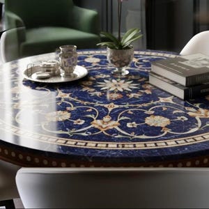 Pu&ograve; includere: Un tavolo rotondo con una superficie blu scuro, ornato da un motivo floreale color crema e oro. Il tavolo ha un bordo in legno ed &egrave; circondato da sedie bianche. Oggetti decorativi e libri sono posizionati sul tavolo.