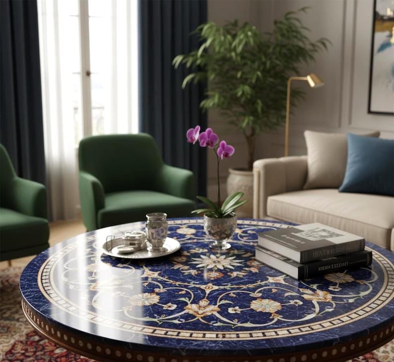 Pu&ograve; includere: Un tavolino rotondo con un piano blu scuro a motivi floreali. Il tavolo ha un bordo in legno ed &egrave; circondato da poltrone verdi, un divano beige e una pianta in vaso. Un piccolo vassoio d'argento e libri sono sul tavolo.
