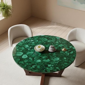 Op de afbeelding: Een ronde salontafel met een malachietgroen blad en een donkerbruine houten basis. Twee witte fauteuils omringen de tafel. Een kleine witte kom met een bloem, een stapel stenen en een goudkleurig object staan op de tafel.