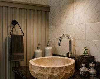 May include: A bathroom sink made of natural stone sits on a dark countertop. The sink is paired with a chrome faucet, soap dispensers, and a small plant. A black light fixture hangs above.