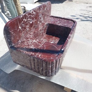 May include: A large, rectangular marble sink with a deep red hue and white veining. The sink features a built-in backsplash and a basin with a rounded edge. The front of the sink has a fluted design.