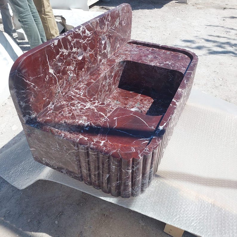 May include: A large, rectangular marble sink with a deep red hue and white veining. The sink features a built-in backsplash and a basin with a rounded edge. The front of the sink has a fluted design.