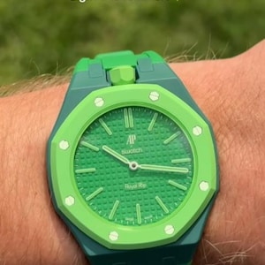 Puede incluir: Un reloj verde y turquesa con esfera verde y bisel verde texturizado. El reloj tiene el texto "AP Swatch Royal Rip" en la esfera. La imagen también incluye el texto "Who's rocking the Green Eight this summer?"