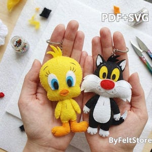 May include: Two felt keychains featuring the cartoon characters Tweety Bird and Sylvester the Cat. The yellow Tweety Bird has blue eyes and orange feet, while the black and white Sylvester has yellow eyes and a red nose. Both include metal rings.