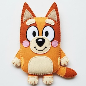 May include: A handmade felt dog toy in orange, tan, and white. The toy has large white eyes, a black nose, and a smiling mouth. It features small pink cheek circles and a small tail.