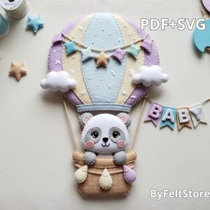 Peut inclure: Montgolfière en feutre avec un panda dans un panier, décorée d'étoiles et de nuages. Le ballon est de couleurs pastel avec le texte "PDF+SVG" et "BABY". Le produit est de ByFeltStore.