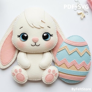 Pode incluir: Um coelho de feltro branco com orelhas, patas e bochechas cor-de-rosa e olhos azuis grandes. O coelho está ao lado de um ovo de Páscoa azul claro e rosa. Os textos "PDF+SVG" e "ByFeltStore" são visíveis.