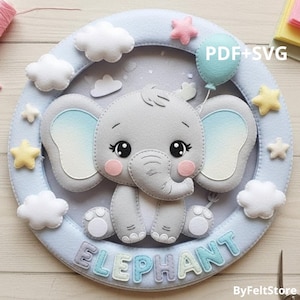 Pode incluir: Decoração de parede em feltro com um elefante cinzento num quadro azul claro. O elefante tem olhos grandes, bochechas cor-de-rosa e segura um balão azul. Nuvens brancas e estrelas pastel circundam o elefante. A palavra "ELEPHANT" está escrita em letras pastel.