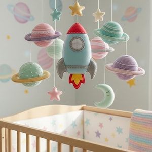 May include: A baby crib with a hanging mobile featuring planets, stars, a rocket, and a crescent moon. The mobile is in pastel colors, with a light blue rocket as the central piece. The crib has a wooden frame and a colorful blanket.