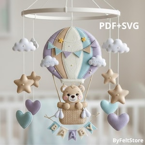 Pode incluir: Móbile de bebê com design de balão de ar quente, urso de pelúcia, nuvens, estrelas e corações em cores pastel. O balão tem um design bege, roxo e azul. Uma faixa abaixo da cesta diz "BABY". O texto "PDF+SVG" é visível.