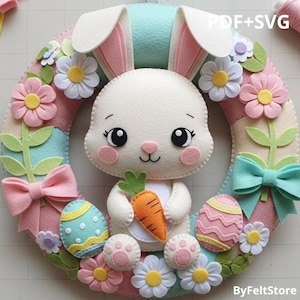 Op de afbeelding: Een handgemaakte paaskrans met een witte konijn die een wortel vasthoudt, omringd door kleurrijke vilten bloemen, strikken en paaseieren. De krans heeft een pastel kleurenschema met de tekst "PDF+SVG" en "ByFeltStore".