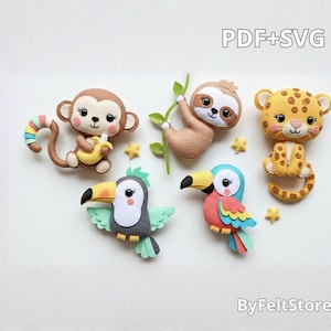 Può includere: Una collezione di ornamenti di animali in feltro, tra cui una scimmia, un bradipo, dei tucani e un leopardo. La scimmia tiene una banana, il bradipo è appeso a un ramo e i tucani hanno becchi colorati. Il testo "PDF+SVG" e "ByFeltStore" sono visibili.