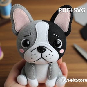 Pode incluir: Um peluche de buldogue francês feito à mão em feltro cinzento, preto, branco e rosa. O cão tem olhos grandes e pretos e uma expressão costurada. O texto "PDF+SVG" está no canto superior direito. O produto é da ByFeltStore.