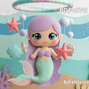 May include: A felt mermaid mobile with a lavender-haired mermaid, holding a coral starfish. The mobile includes hanging felt starfish, seashells, and spheres. The background features a sea-themed design with the text "PDF+SVG" and "ByFeltStore".