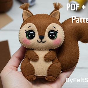 Pode incluir: Um esquilo de feltro feito à mão com corpo castanho, barriga bege e cauda fofa. O esquilo tem olhos grandes e expressivos com íris verdes e bochechas rosadas. O texto na imagem diz "PDF + SVG Pattern" e "ByFeltStore".