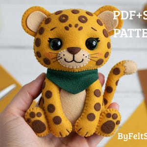 Pode incluir: Um filhote de leopardo de feltro feito à mão com corpo amarelo, manchas marrons e um lenço verde. O brinquedo de pelúcia tem olhos grandes e pretos e um rosto sorridente. O texto na imagem diz "PDF+SVG PATTERN" e "ByFeltStore".