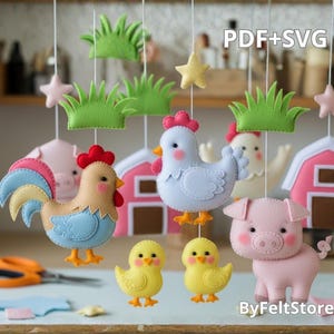 Pode incluir: Um mobile de fazenda de feltro feito à mão com um galo, uma galinha, um porco, pintinhos e celeiros. O mobile inclui grama verde, estrelas rosa e é suspenso por fios brancos. Os textos "PDF+SVG" e "ByFeltStore" são visíveis.