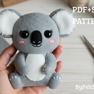 May include: A handmade gray felt koala bear plushie with white accents on the ears and chest, black eyes, and pink cheeks. The koala is being held in a hand. Text on the image reads "PDF+SVG PATTERN" and "ByFeltStore".