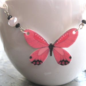 Pink butterfly pendant necklace, a delicate necklace, with white butterfly charms and a pink-and-black centerpiece.