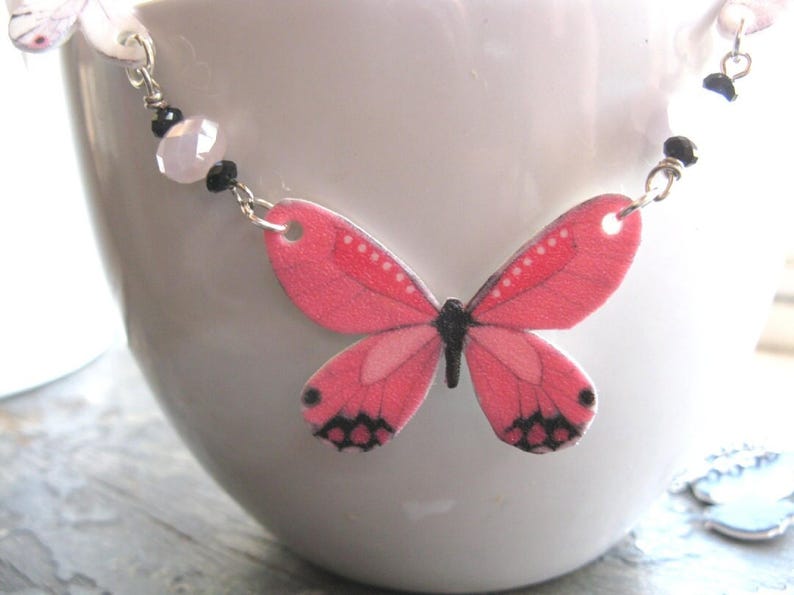 Pink butterfly pendant necklace, a delicate necklace, with white butterfly charms and a pink-and-black centerpiece.