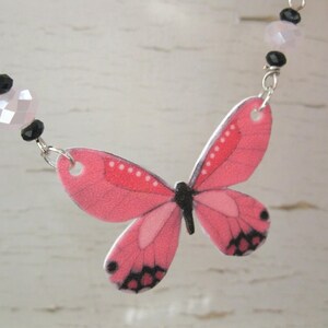 Pink butterfly pendant necklace, a delicate necklace, with white butterfly charms and a pink-and-black centerpiece.