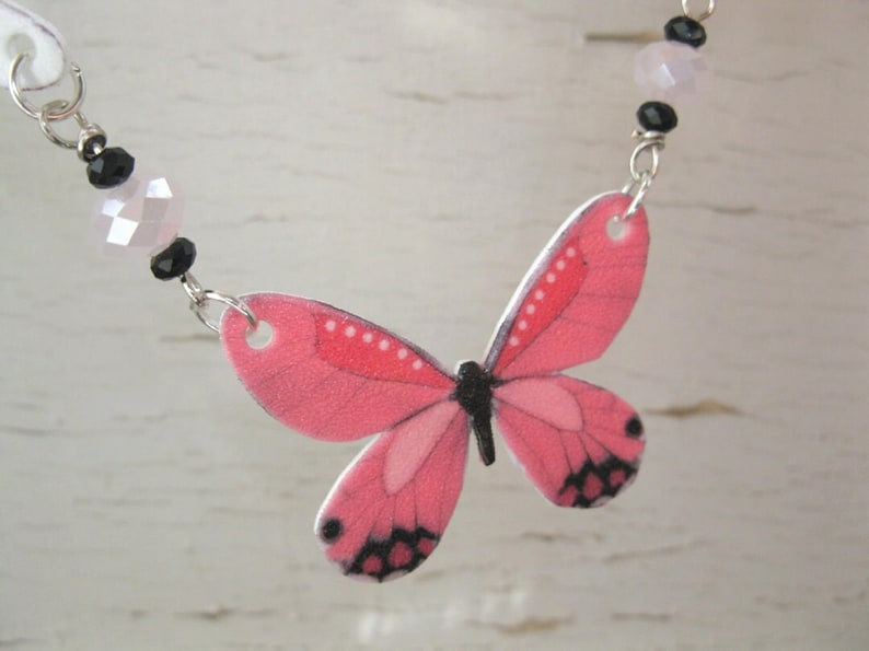 Pink butterfly pendant necklace, a delicate necklace, with white butterfly charms and a pink-and-black centerpiece.
