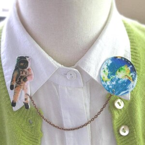 Astronaut and Earth globe double pin from outer space, linked by a celestial chain—space pin duo