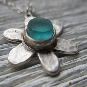 Handmade sea glass flower pendant necklace with aqua blue and other colours in a cabochon in a five-petal silver setting on a silver chain.