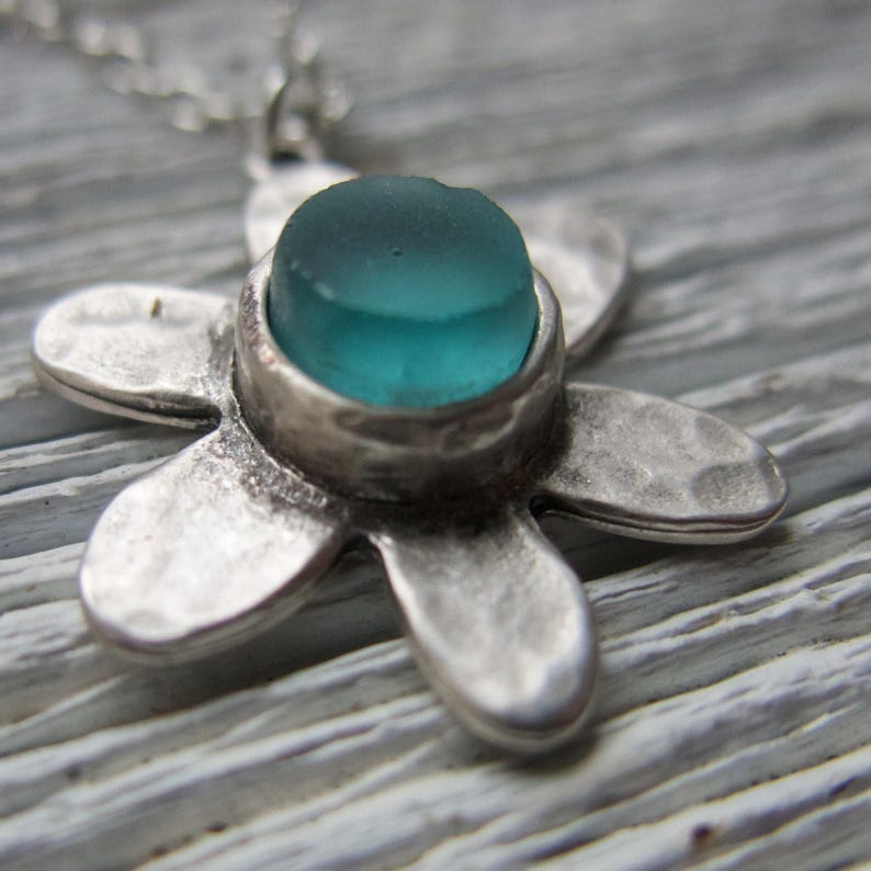 Handmade sea glass flower pendant necklace with aqua blue and other colours in a cabochon in a five-petal silver setting on a silver chain.
