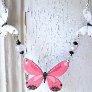 Pink butterfly pendant necklace, a delicate necklace, with white butterfly charms and a pink-and-black centerpiece.