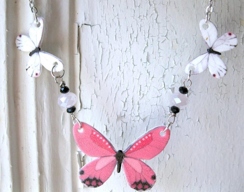 Pink butterfly pendant necklace, a delicate necklace, with white butterfly charms and a pink-and-black centerpiece.