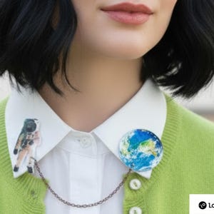 Astronaut pin with planet Earth pin linked by copper celestial chain on a white shirt collar — space pin duo.
