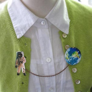 Astronaut and Earth globe double pin from outer space, linked by a celestial chain—space pin duo