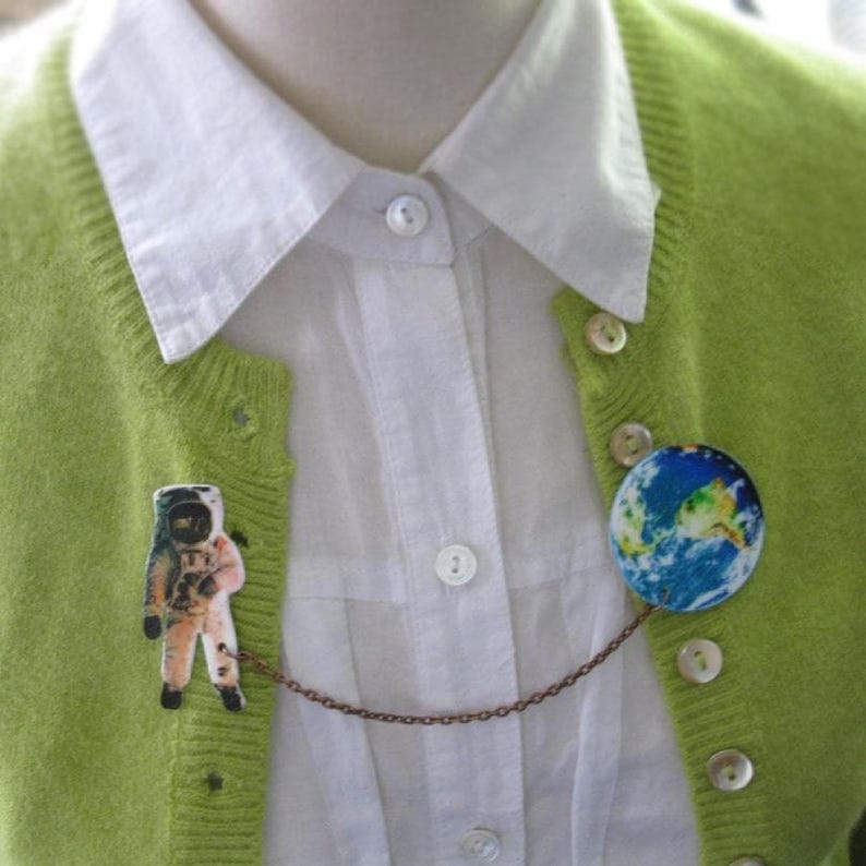 Astronaut and Earth globe double pin from outer space, linked by a celestial chain—space pin duo