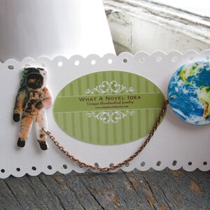 Astronaut and Earth globe double pin from outer space, linked by a celestial chain—space pin duo