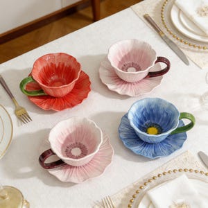 Könnte beinhalten: Ein Set aus drei Keramikbechern mit gesprenkelter, matter Oberfläche. Die Becher sind in Creme-, Hellgrau- und Dunkelgrautönen gehalten. Jeder Becher hat ein schlichtes, modernes Design und einen abgerundeten Griff.