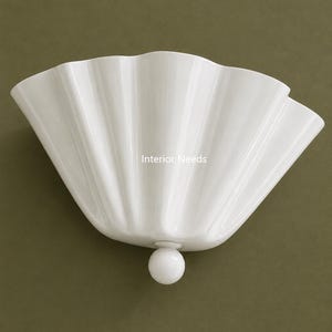 May include: A white, scalloped wall sconce with a spherical base. The sconce has a fan-like shape with vertical ridges and the text "Interior Needs". The fixture is mounted on a muted green wall.