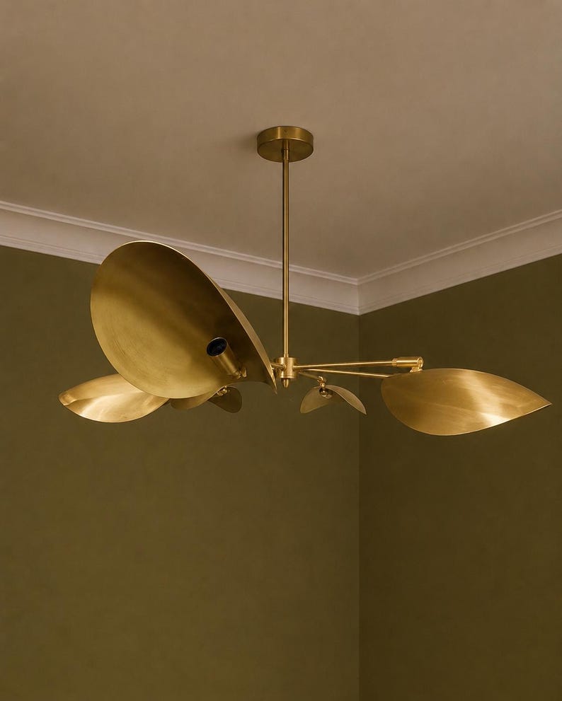 May include: A brass chandelier featuring multiple curved, leaf-shaped metal shades extending from a central rod. The fixture has a metallic gold finish and includes exposed light bulb sockets positioned within the concave surfaces of the shades.