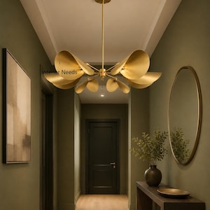 May include: A gold-toned metal chandelier featuring multiple trumpet-shaped shades arranged in a radial pattern, suspended from a central rod. The fixture includes the text Interior Needs printed on one of the metallic shades in black lettering.
